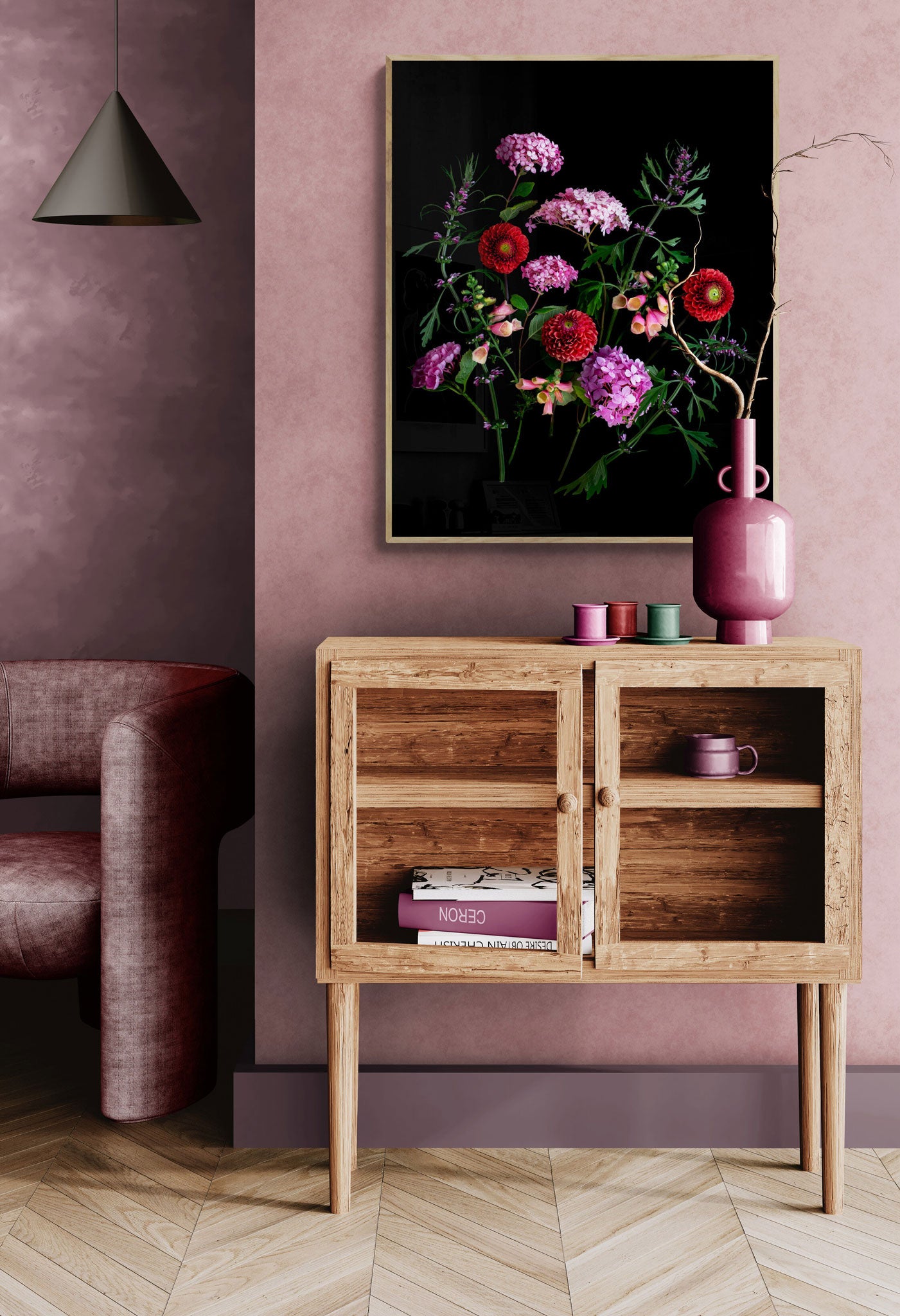 A framed floral art print with vibrant pink, red, and purple flowers on a black background, displayed on a dusty pink wall above a wooden sideboard in a styled room.