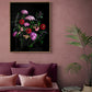 A framed floral wall art print hangs above a bed in a styled bedroom. The artwork shows a bouquet of pink, red, and purple flowers on a black background, with a gold-toned frame.