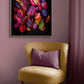 A framed wall art print featuring a cluster of colorful autumn leaves on a black background, displayed above a yellow textured armchair with a purple pillow in a styled room setting.