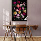 Framed dark botanical print of different coloured roses photographed on a black background hung on a pale pink coloured wall.