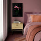 A framed wall art print featuring peach pink double tulips with Ranunculus  on a black background, styled in a bedroom setting above a wooden nightstand next to a bed with dusty rose bedding and a rust-colored throw blanket.